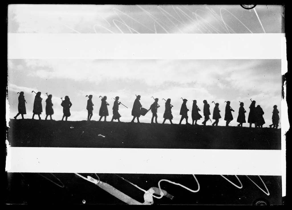 Black and white photograph silhouette of group of figures in a line carrying tools.